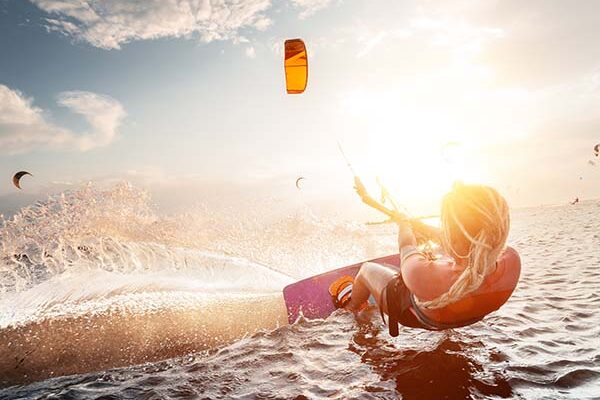 Professional kite surfer woman rides on a board with a plank in her hands on a leman lake with sea water at sunset. Water splashes and sun glare. Water sports stage kitesurf martinique